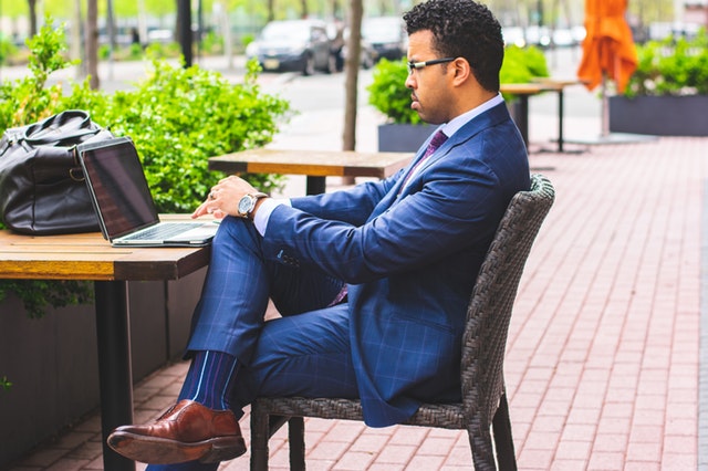 Muž v modrom obleku sedí za stolom a píše na počítači